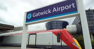 Gatwick Airport entrance sign with a red train passing in front of the terminal building.