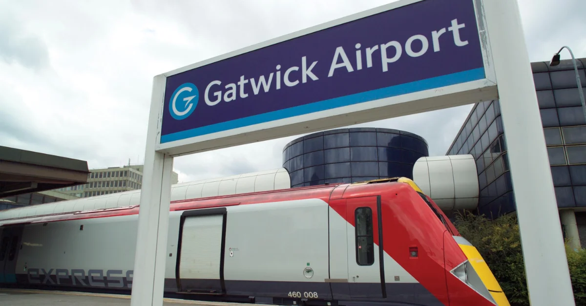 Gatwick Airport entrance sign with a red train passing in front of the terminal building.