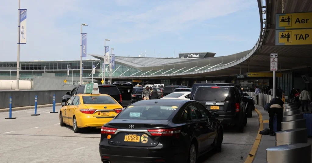 Airport terminal drop-off area with taxis and cars lined up outside the departures entrance.