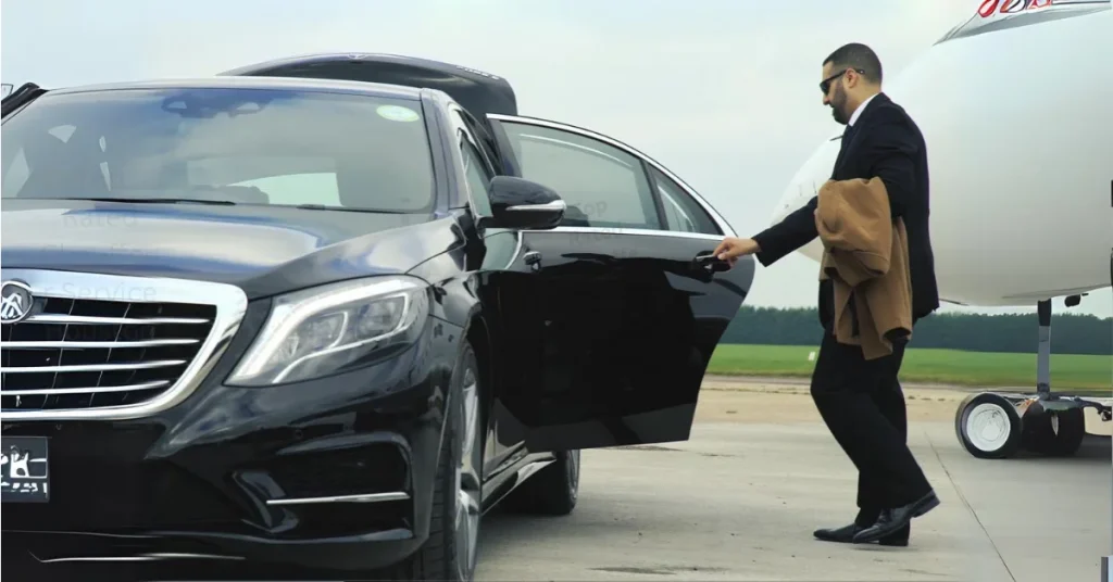 Chauffeur opening the door of a black luxury car beside a private jet on an airport runway.